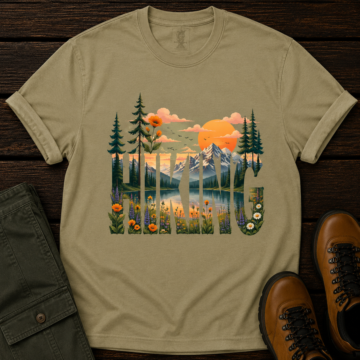 Beige t-shirt with nature-themed design featuring mountains, trees, and flowers on a wooden surface.
